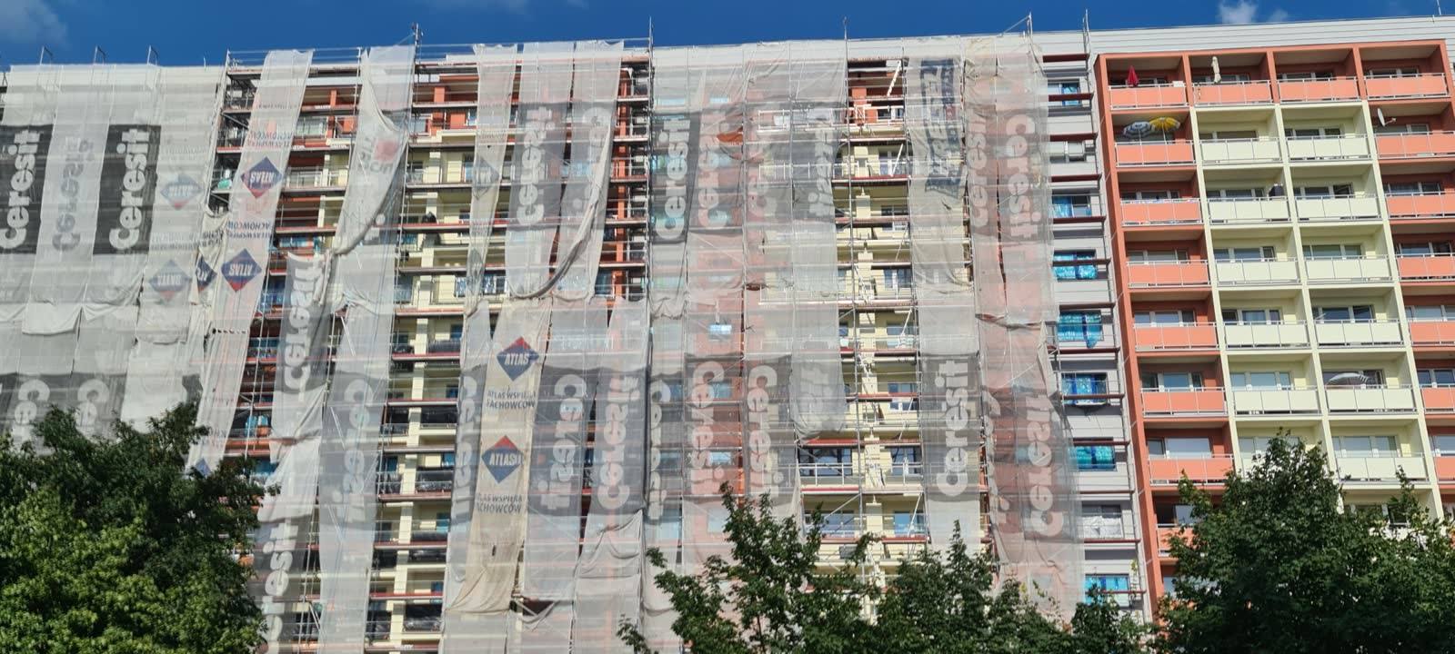 Docieplenie elewacji bloku wielorodzinnego w Elblągu-Zakrzewie — budynek w rusztowaniach z siatką ochronną