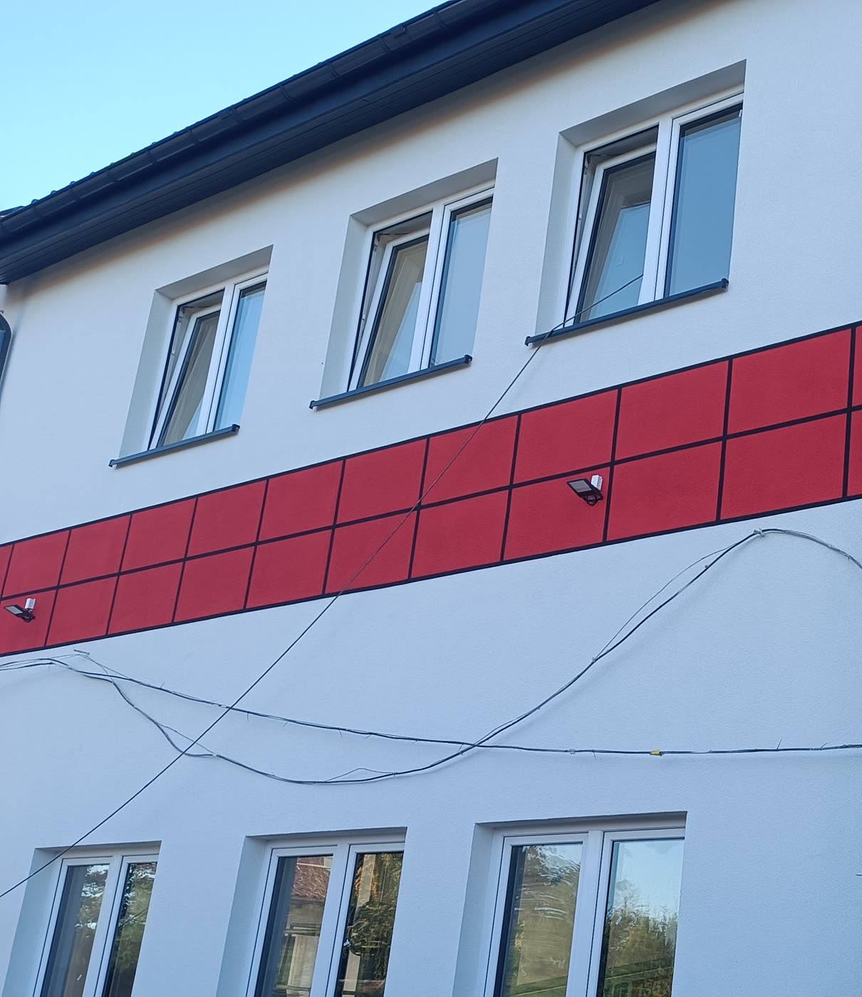 Elewacja budynku OSP Łęcze po remoncie — biały tynk, czerwony pas z płyt elewacyjnych i nowe okna
